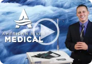 Man in business attire speaking next to medical equipment with blue background and play button overlay