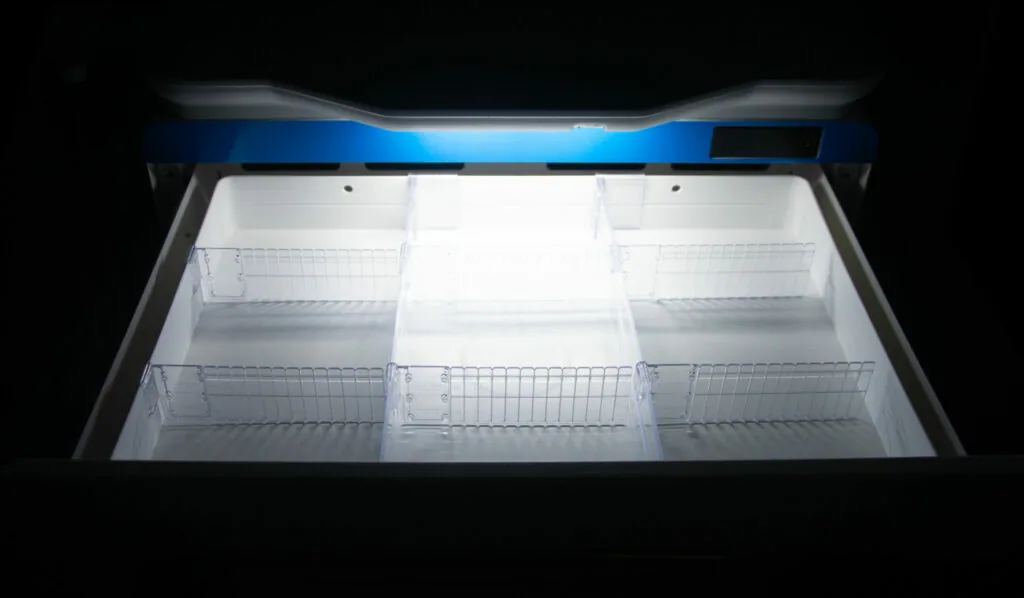 Open chest freezer with blue top and empty wire baskets viewed from above against black background