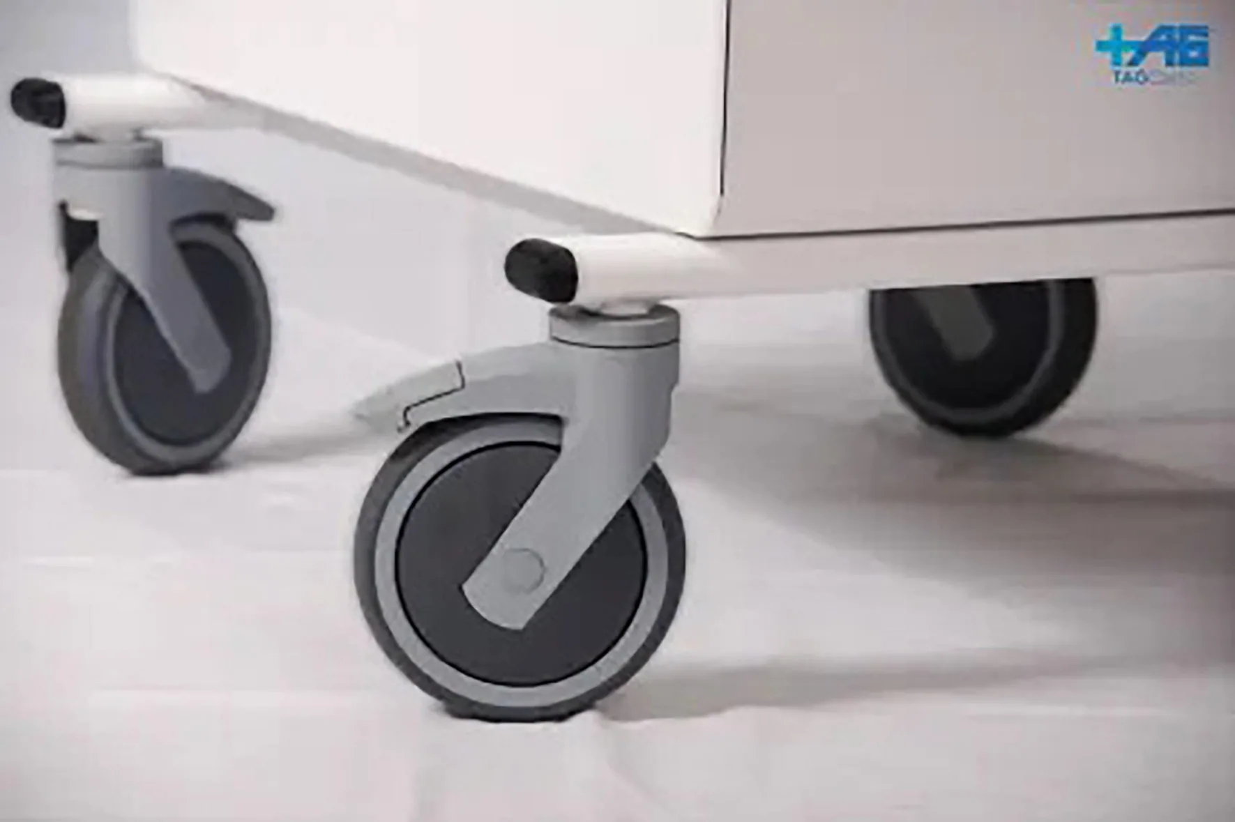 Three industrial casters with gray stems and black wheels beneath white equipment on polished floor.